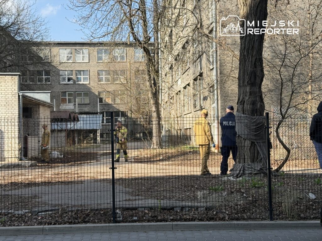 Strażacy i policjanci prowadzą działania ratunkowe przy opuszczonym budynku z przeszkloną fasadą.