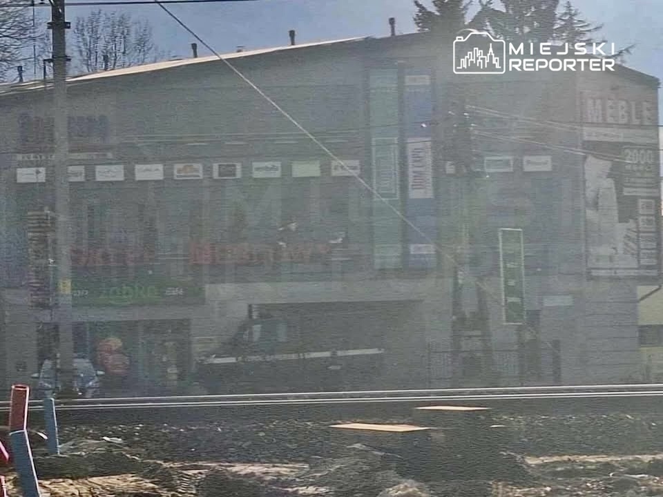 Nowoczesny budynek z przeszkloną fasadą i reklamami, w tle widoczne tory kolejowe oraz elementy budowy.