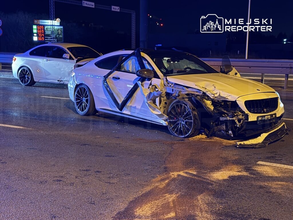 Dwa uszkodzone białe samochody osobowe na drodze, jeden z widocznymi poważnymi zniszczeniami z przodu.