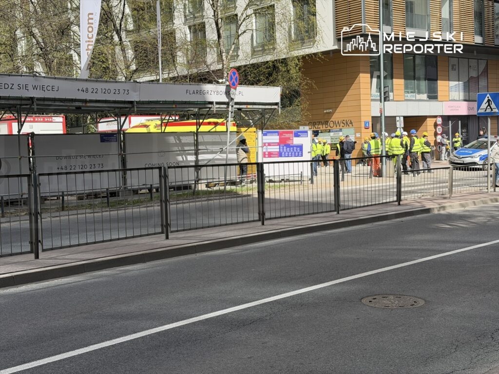 Grupa pracowników w kamizelkach odblaskowych omawia prace budowlane przed nowoczesnym biurowcem.