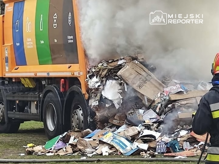 Śmieciarka wypełniona odpadami, z unoszącym się dymem, podczas akcji gaszenia pożaru.