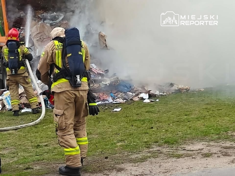 Strażacy gaszą pożar wśród stosu odpadów w otwartym terenie, w tle widoczna gęsta chmura dymu.