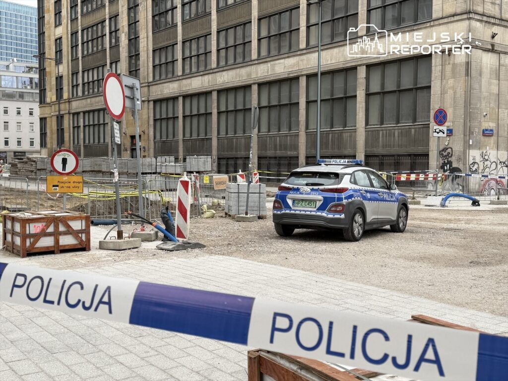 Policyjny radiowóz zaparkowany na placu budowy, otoczony barierkami i znakami drogowymi.