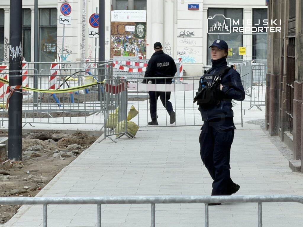 Policjant w mundurze patroluje teren budowy, otoczony barierkami i taśmami ostrzegawczymi.