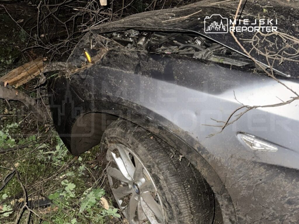 Samochód osobowy wjeżdżający w zarośla, z widocznymi uszkodzeniami i błotem na karoserii.