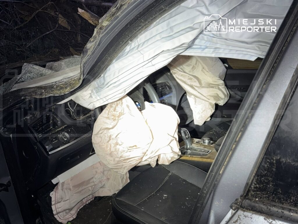 Wnętrze rozbitego samochodu z rozwiniętymi poduszkami powietrznymi i uszkodzonym kokpitem.