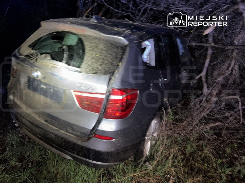 Samochód osobowy marki BMW zaparkowany w zaroślach, pokryty kurzem i brudem, z uszkodzoną tylną szybą.
