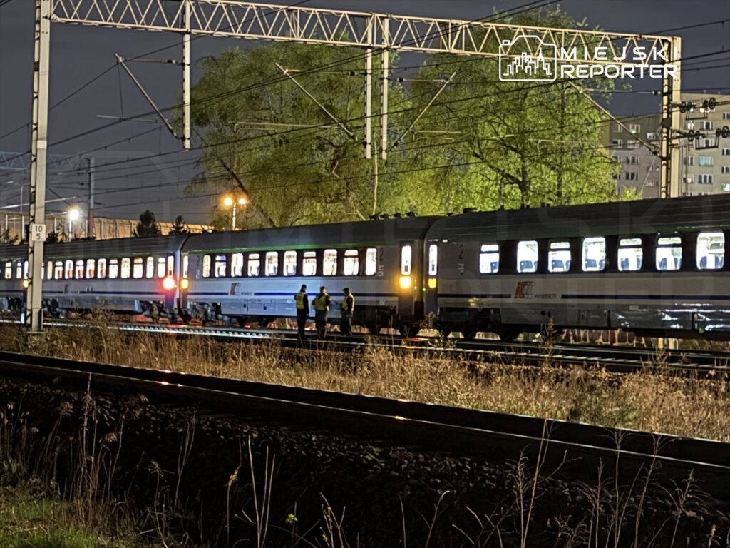 Czterej pracownicy w odblaskowych kamizelkach sprawdzają pociąg osobowy na stacji kolejowej w nocy.