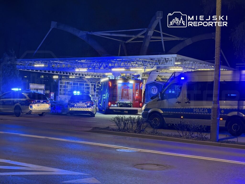 Nocna akcja służb ratunkowych z wozem strażackim oraz radiowozami policyjnymi na terenie stacji.