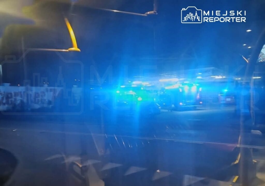 Nocna scena z włączonymi sygnalizatorami świetlnymi pojazdów służb ratunkowych na parkingu.