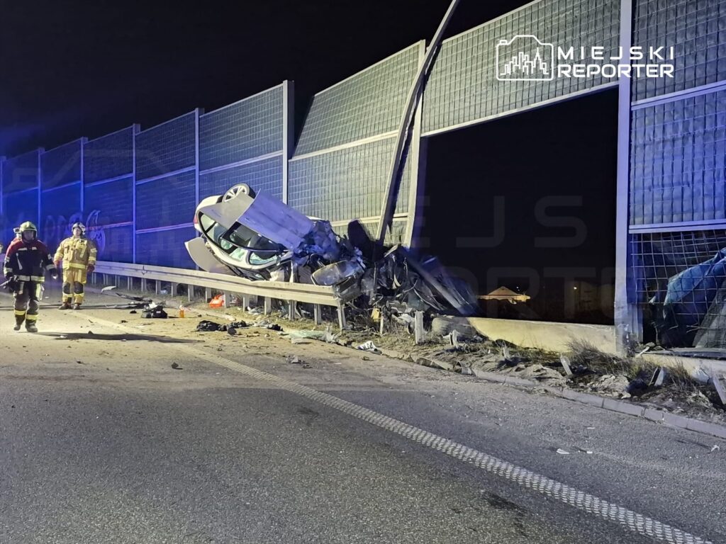 W nocy na drodze leży przewrócony samochód, a obok niego strażacy w sprzęcie ochronnym.