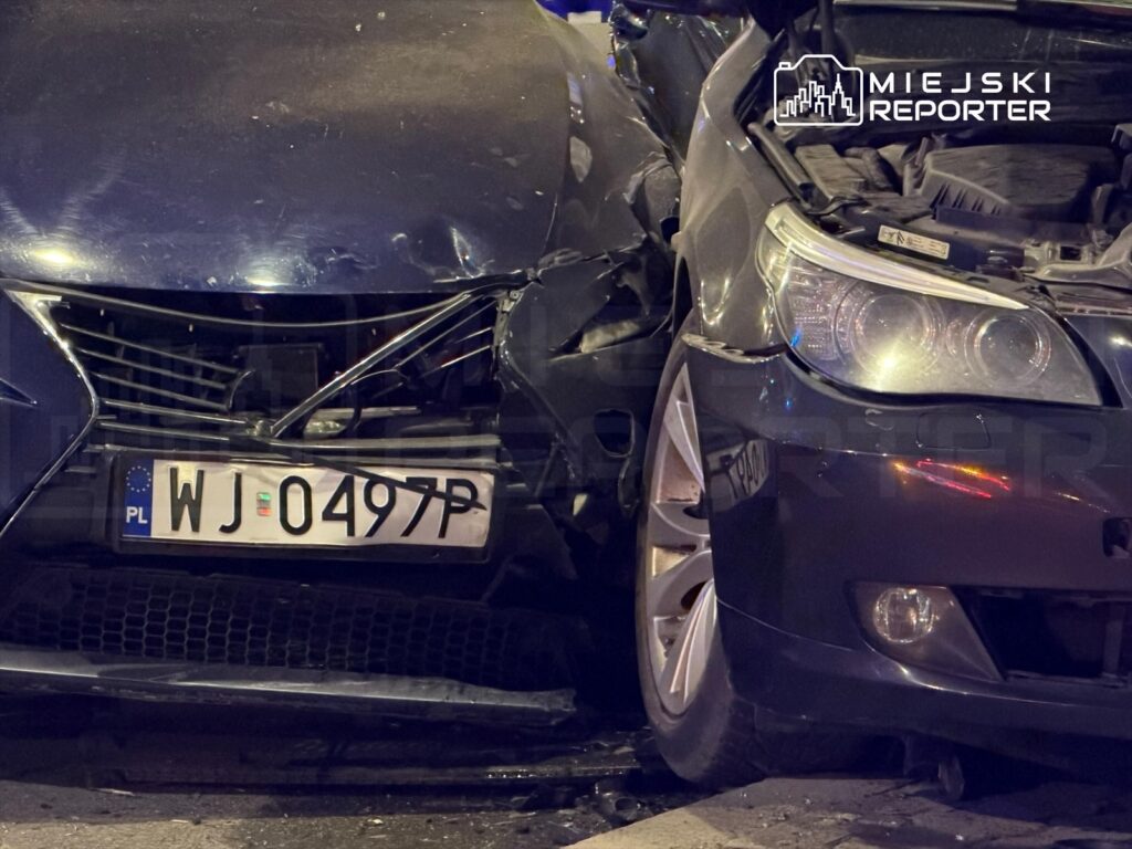 Dwa uszkodzone samochody osobowe zderzone na ulicy, widoczny zniszczony przód jednego z pojazdów.