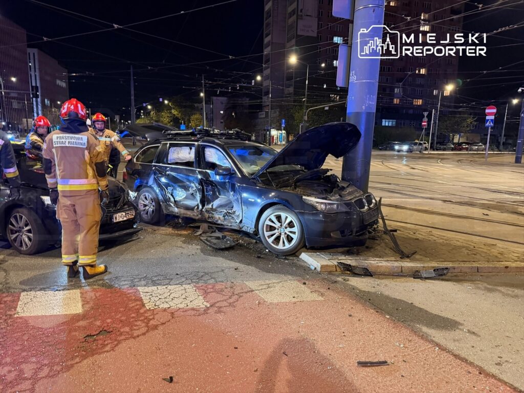 Strażacy w mundurach przeprowadzają akcję ratunkową przy zderzeniu dwóch samochodów osobowych na ulicy nocą.