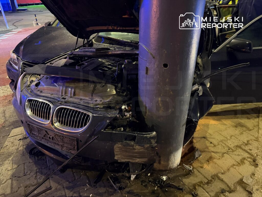 Uszkodzony samochód osobowy zderzony z metalowym słupem na oświetlonej ulicy.