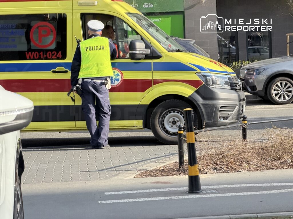 Policjant w kamizelce odblaskowej rozmawia z kierowcą karetki na ulicy w mieście.