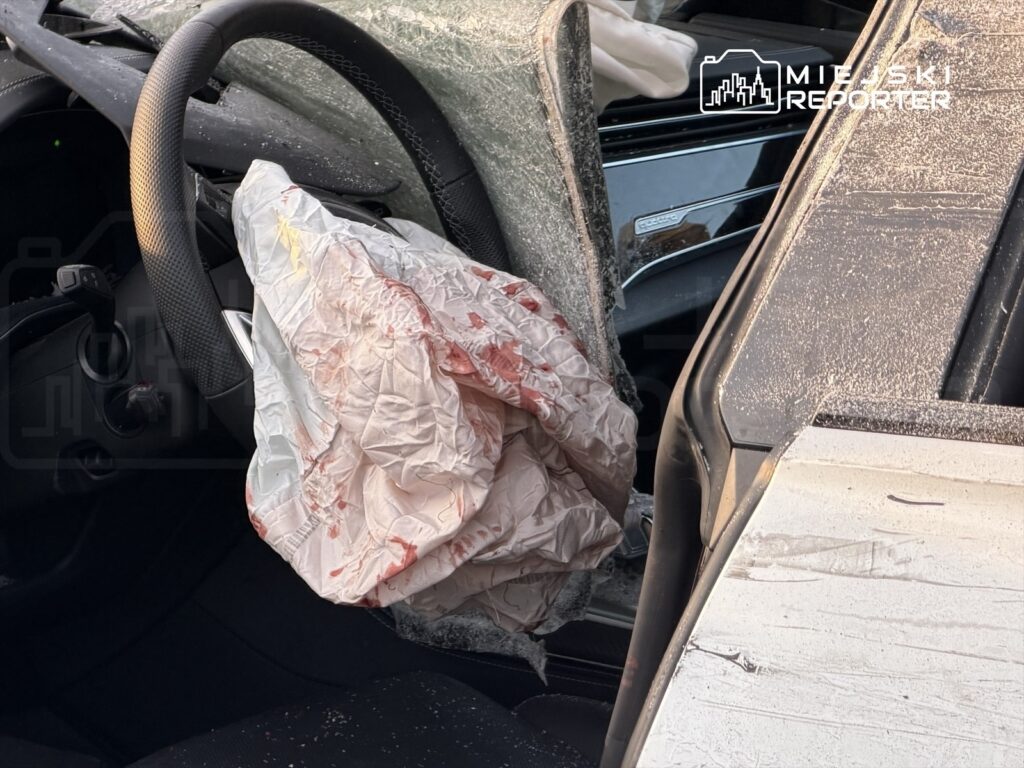 Zdeformowana kierownica samochodu z wystrzeloną poduszką powietrzną, widoczna plama krwi na tkaninie.