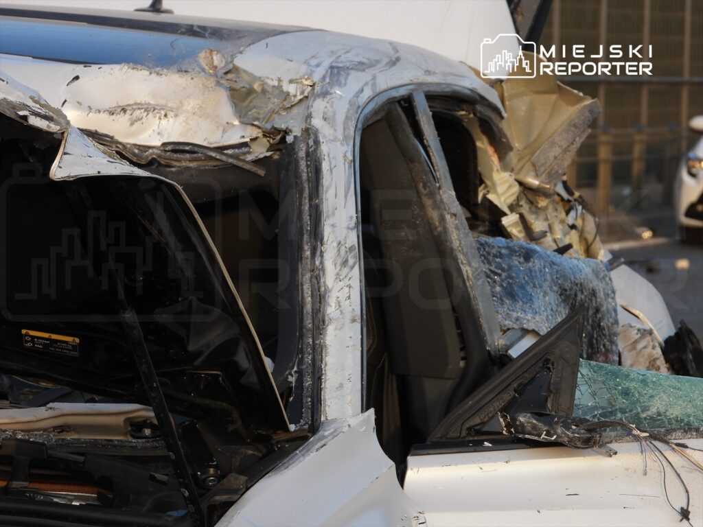 Zniszczony pojazd osobowy z uszkodzoną karoserią i rozbitą szybą, stojący na parkingu.