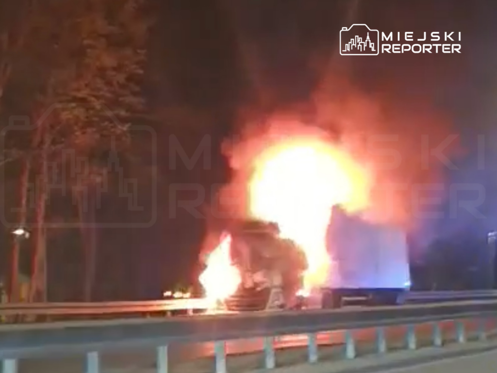 Ogień wydobywający się z tylnej części ciężarówki na drodze, w otoczeniu drzew i nocnego nieba.