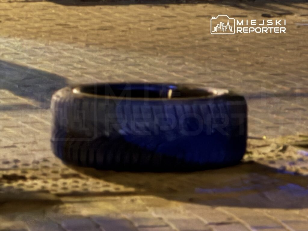 Czarna opona leży na brukowanej nawierzchni, otoczona delikatnym światłem ulicznym.