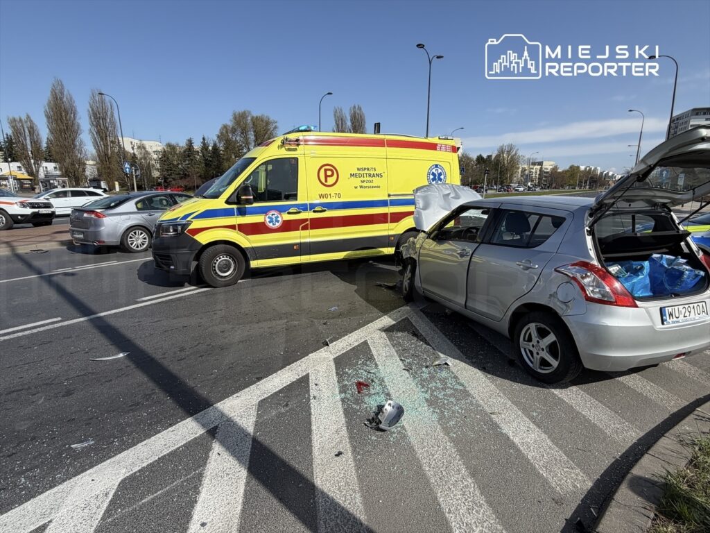 Karetka pogotowia stojąca obok uszkodzonego srebrnego samochodu osobowego na ruchliwej ulicy.