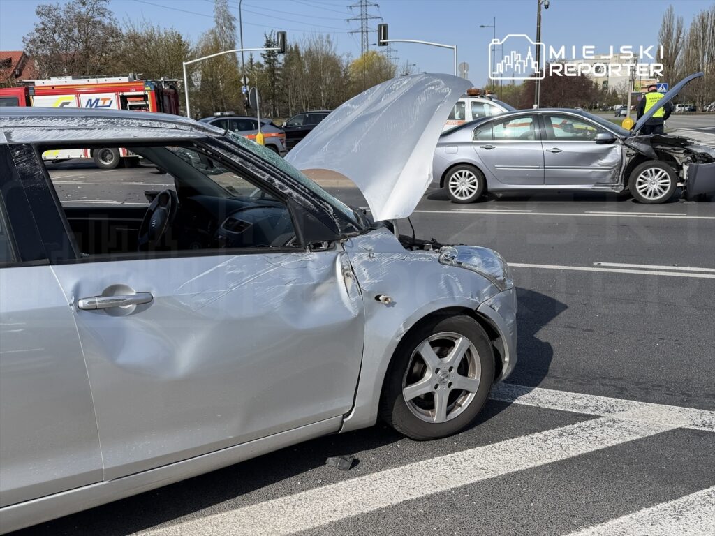 Zderzone samochody na skrzyżowaniu, jeden z pojazdów ma otwartą maskę, a drugi uszkodzoną przednią część.