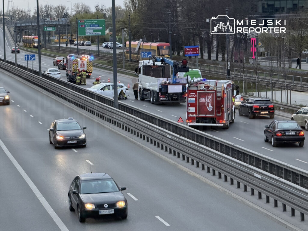 Na drodze odbywa się akcja ratunkowa, w której uczestniczą strażacy oraz karetka, obok unieruchomione pojazdy.