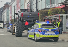 Wielki samochód terenowy z ogromnymi oponami stoi na drodze, obok policyjny radiowóz oraz kilka osób w kamizelkach odblaskowych.