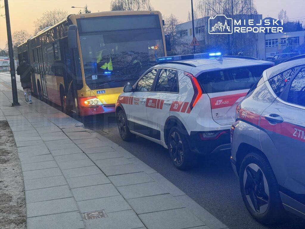 Mężczyzna w czarnej odzieży biegnie w kierunku autobusu, obok parkują samochody z oznaczeniem służb miejskich.