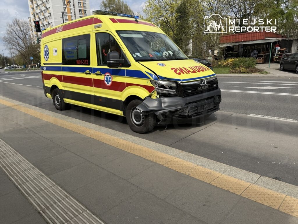 Karetka pogotowia z uszkodzeniem przodu zatrzymana na przystanku w miejskim otoczeniu.