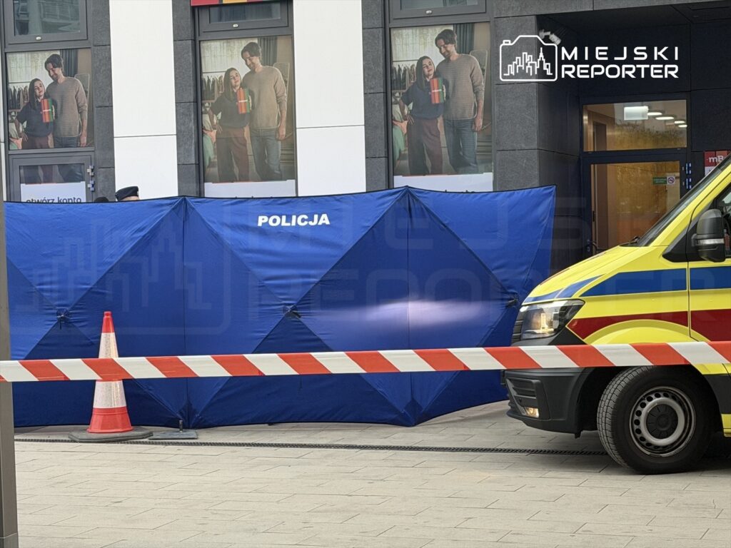 Policja zabezpiecza teren niebieską namiotem w pobliżu karetki, z widoczną taśmą ostrzegawczą.