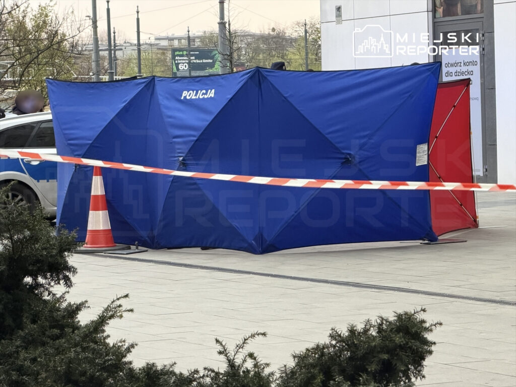Niebieski namiot policyjny ustawiony na placu, z oznaczeniem "POLICJA", otoczony taśmą zabezpieczającą.