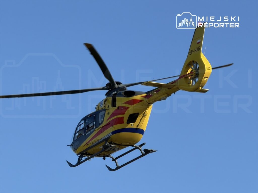 Żółty śmigłowiec ratunkowy przelatuje nad błękitnym niebem.