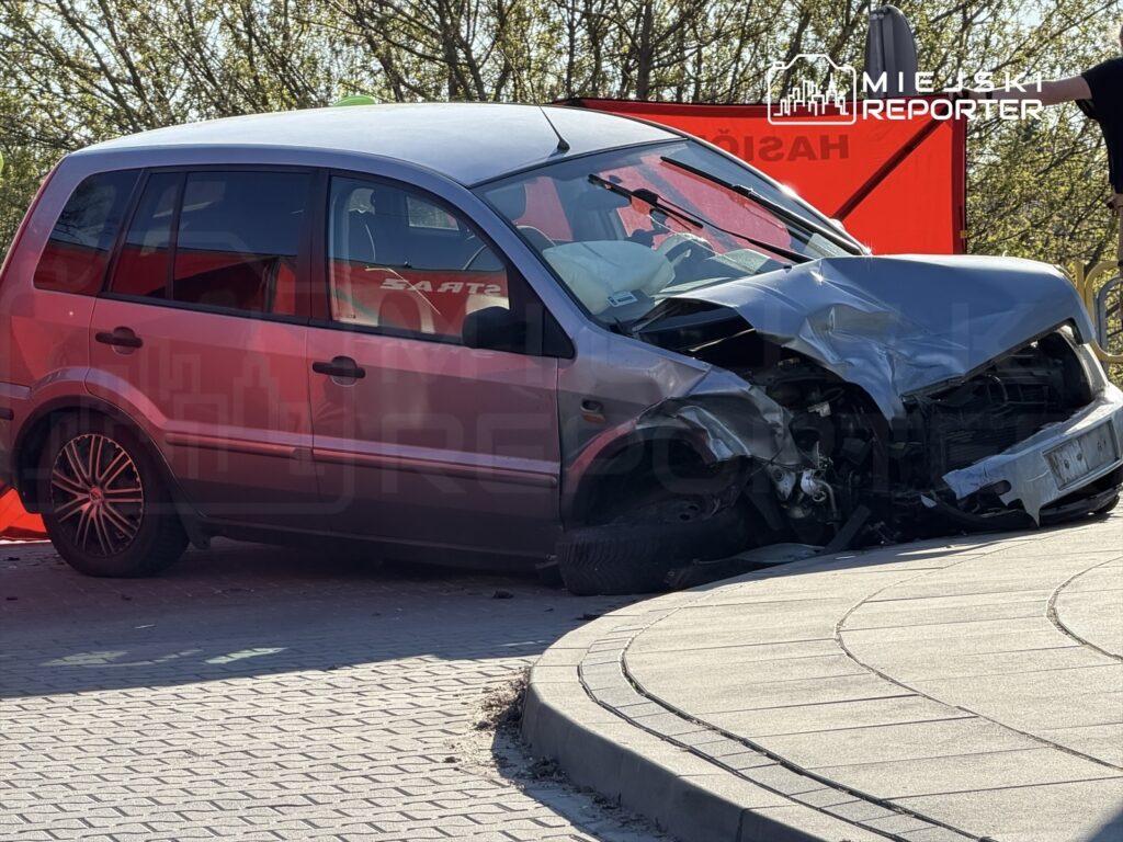 Zniszczony samochód osobowy z wgniecionym przodem stoi na chodniku, obok oznakowanie sytuacji kryzysowej.