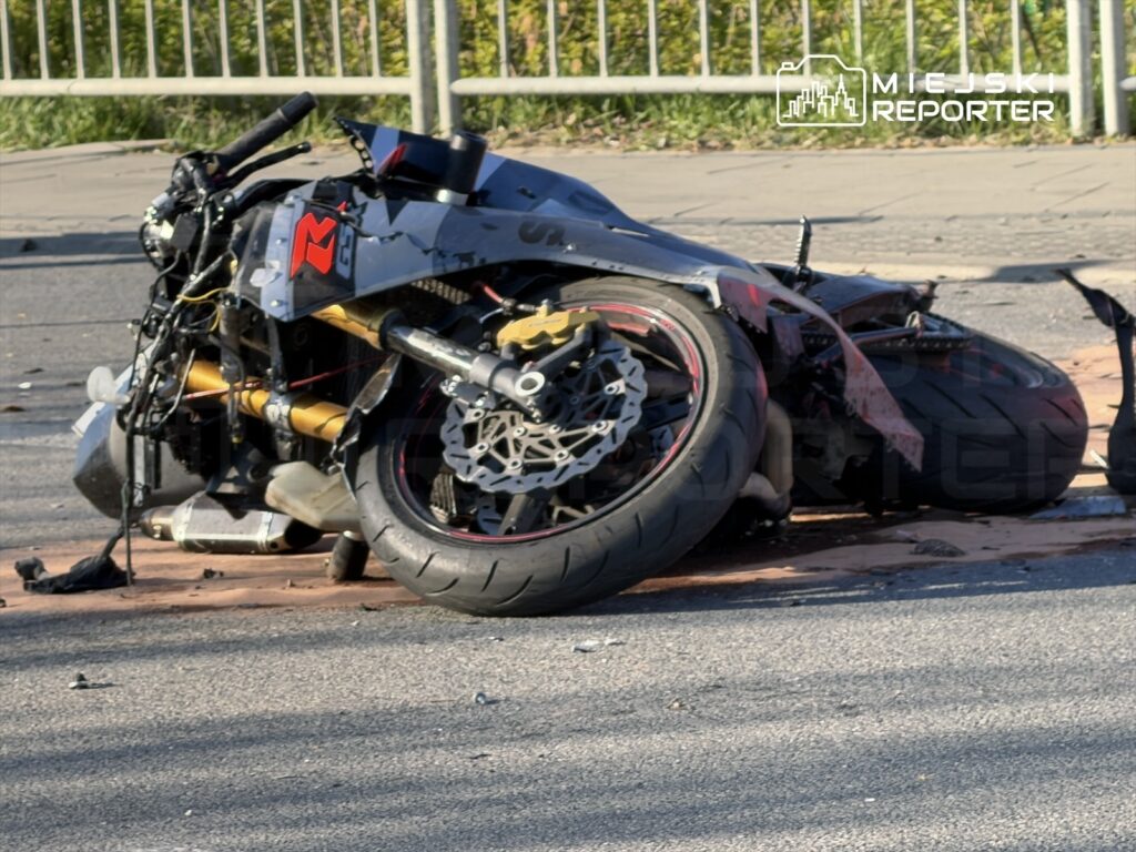 Zniszczony motocykl leży na jezdni, otoczony fragmentami asfaltu i metalowymi elementami.