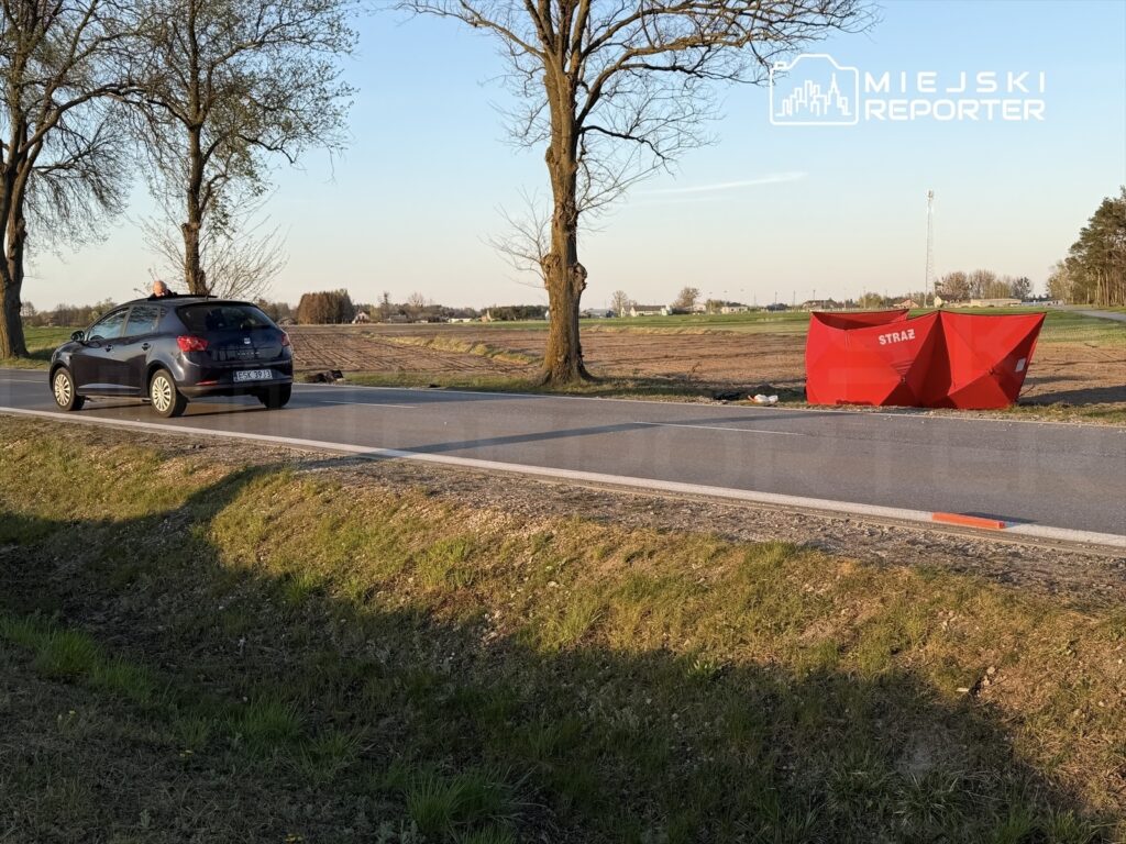 Czarny samochód osobowy stoi przy drodze, obok czerwony namiot strażacki na polu w słoneczny dzień.