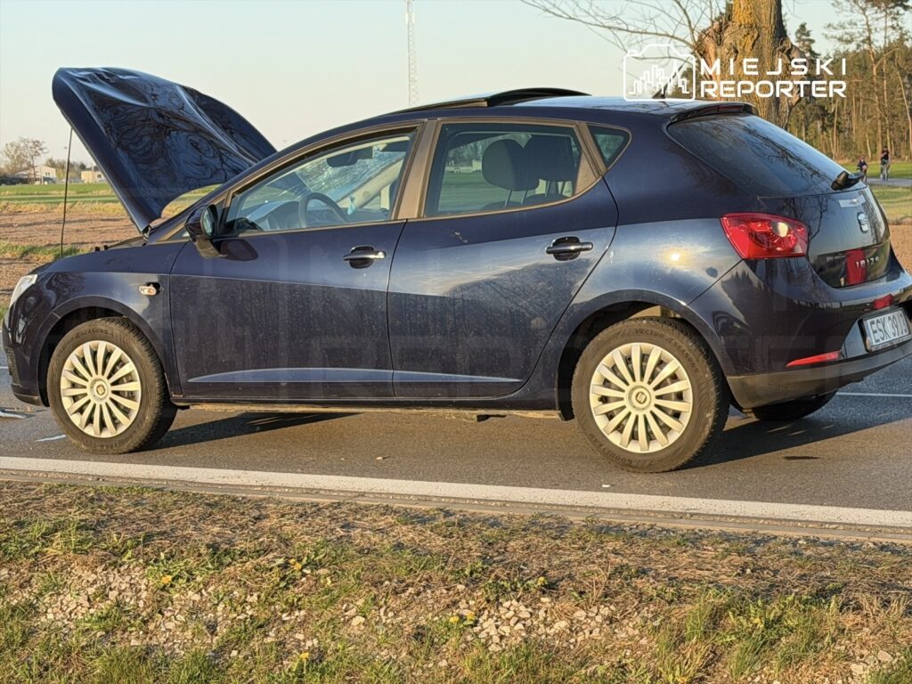 Czarny samochód osobowy z otwartą maską stoi na poboczu drogi w słoneczny dzień.