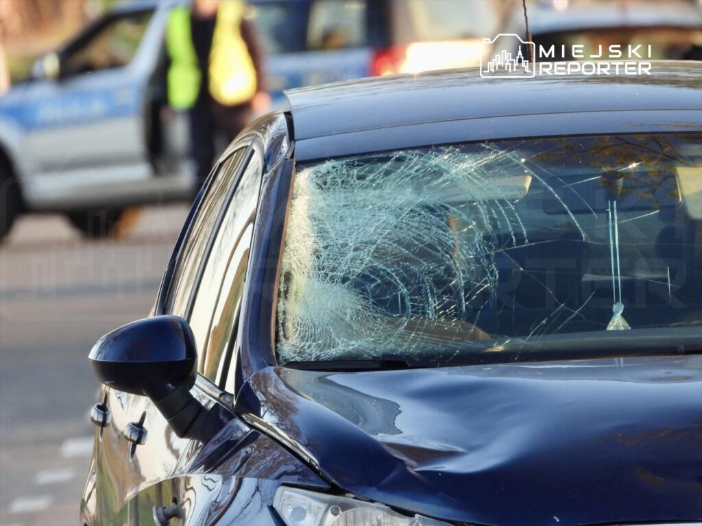 Zniszczony samochód z pękniętą szybą przednią na tle policyjnych pojazdów.
