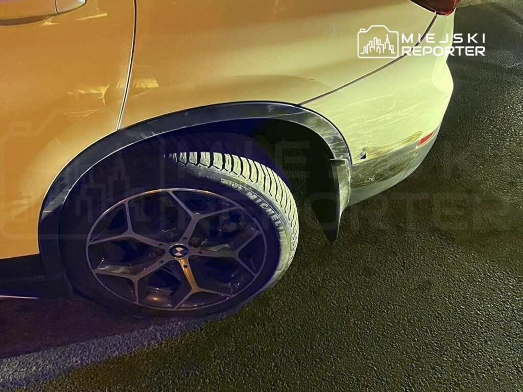 Złoty samochód osobowy z widocznymi zarysowaniami na nadwoziu i stylowymi felgami, zaparkowany na ciemnej nawierzchni.