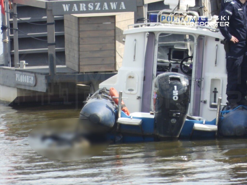 Policyjna łódź patrolowa z funkcjonariuszami na pokładzie zatrzymana obok pływającego obiektu w wodach miejskich.