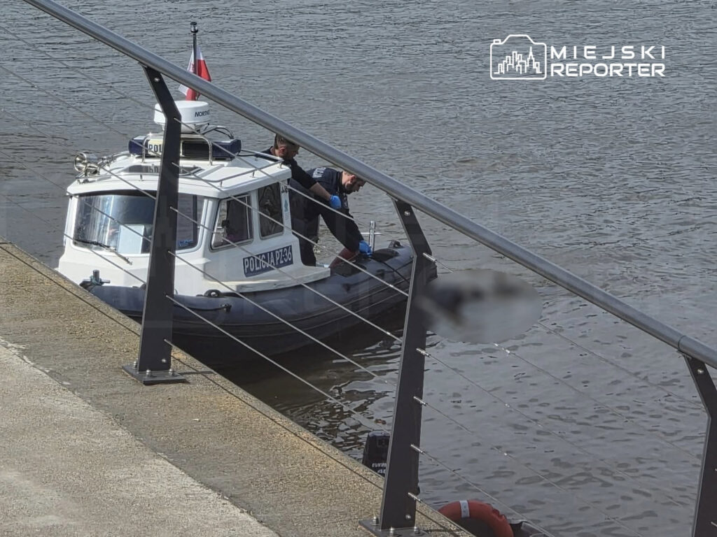 Dwóch policjantów na łodzi patrolowej "POLICJA PZ-36" przeszukuje nabrzeże wzdłuż rzeki.