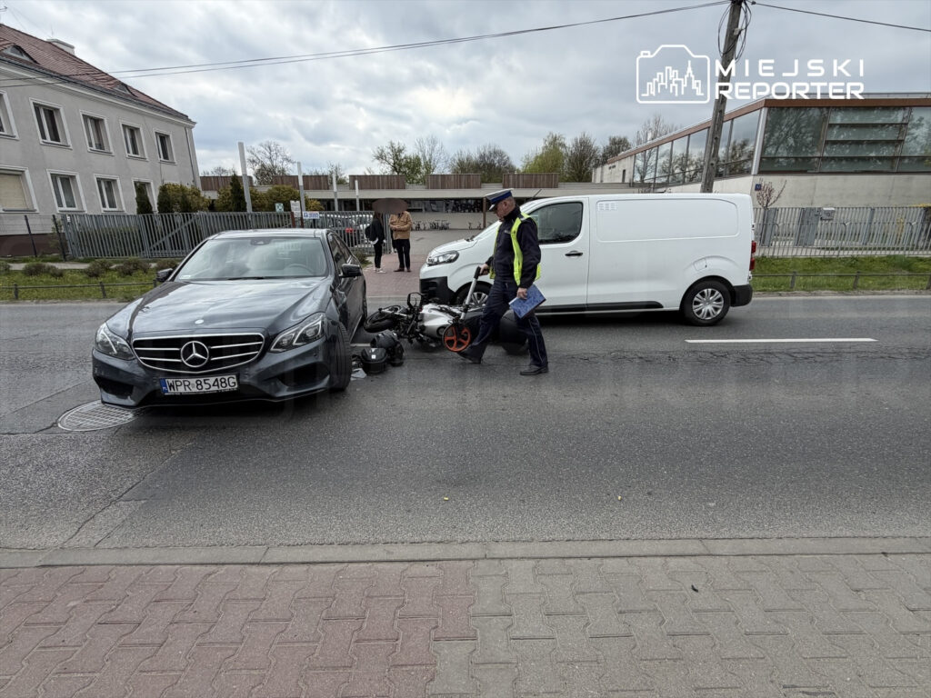 Policjant bada wypadek drogowy obok uszkodzonego samochodu osobowego i dostawczego na ruchliwej ulicy.