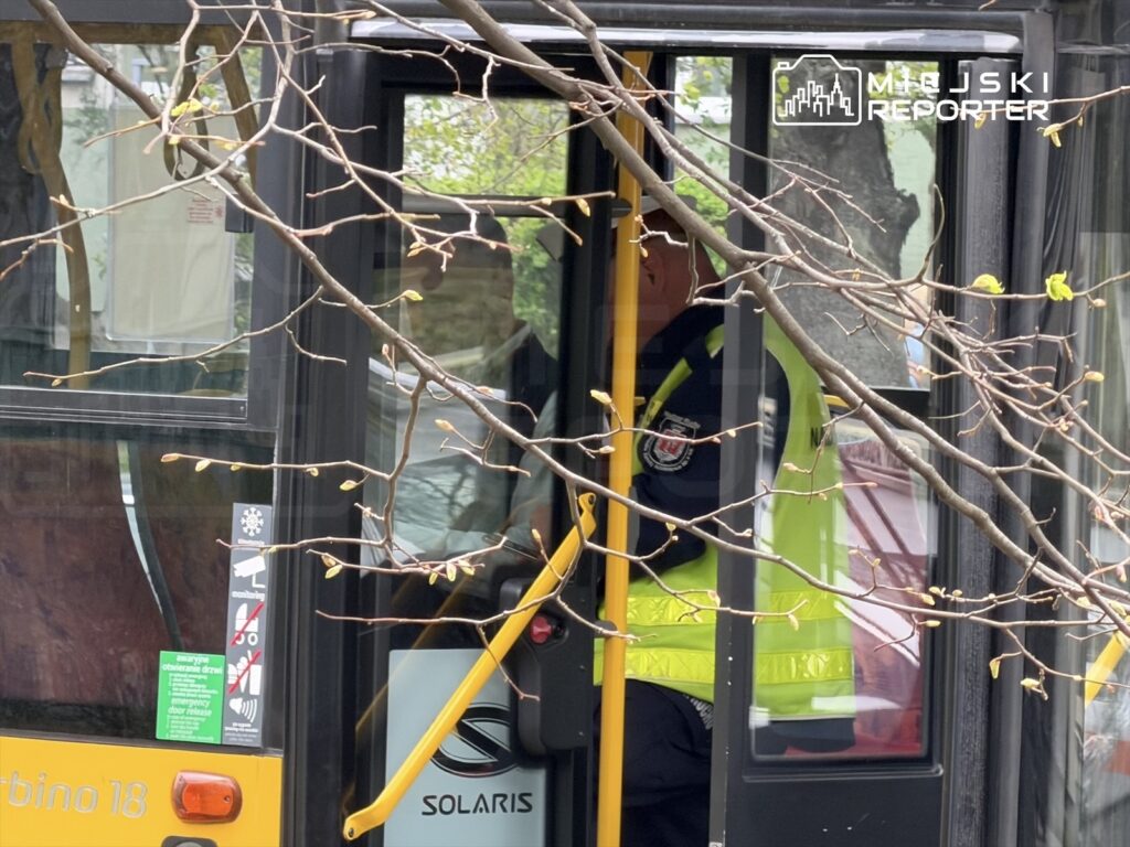 Kierowca autobusu miejskiego w żółtej kamizelce siedzący za sterami pojazdu z otwartymi drzwiami.