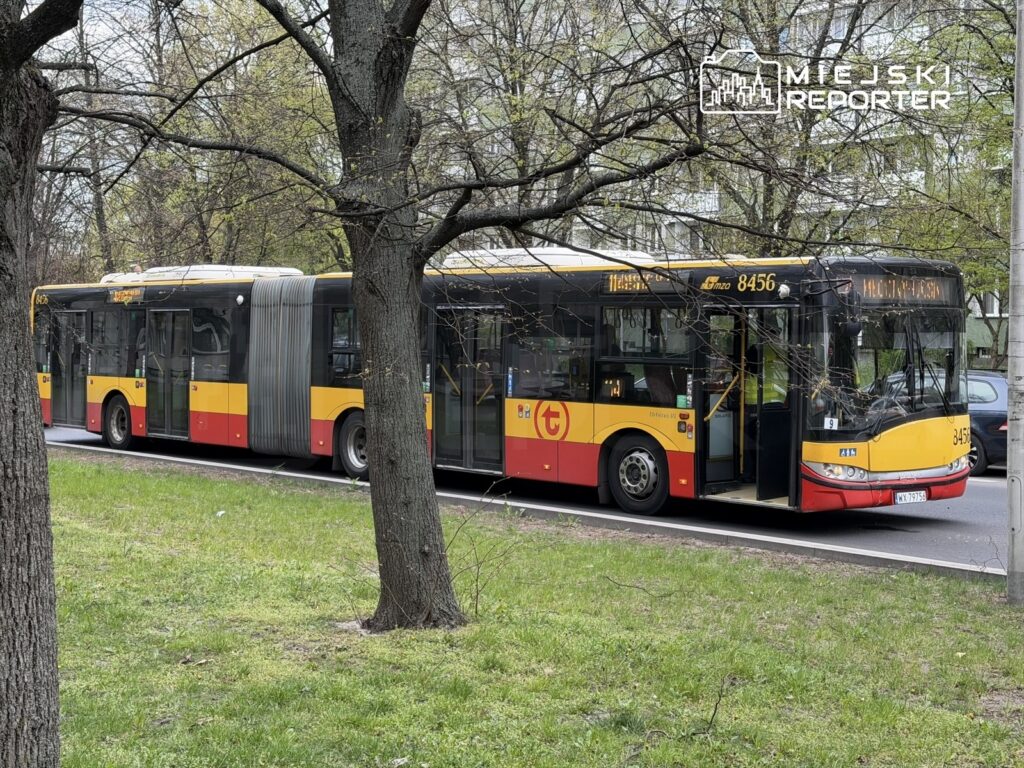 Autobus miejski z numerem 8456 zatrzymany na przystanku wśród drzew w miejskim otoczeniu.