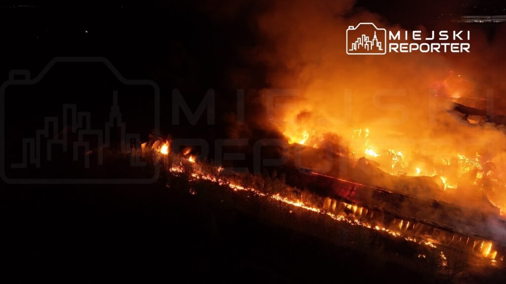 Intensywne płomienie ognia trawią teren w nocy, otoczony gęstym dymem i ciemnością.