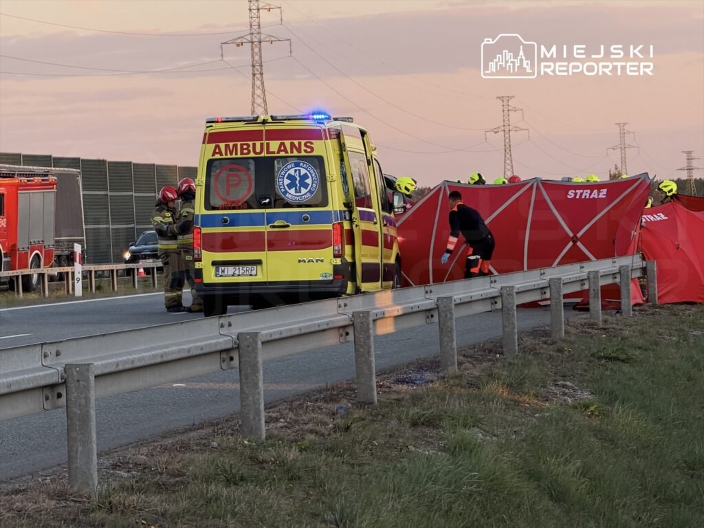 Ratownicy medyczni przygotowują sprzęt obok karetki na poboczu drogi, zabezpieczając miejsce zdarzenia.