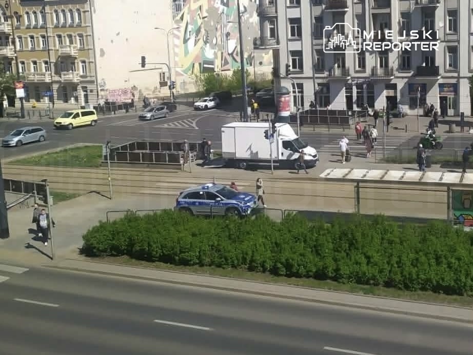 Policyjny radiowóz zatrzymany na ulicy obok białego furgonu, w tle ruchliwa ulica i budynki mieszkalne.