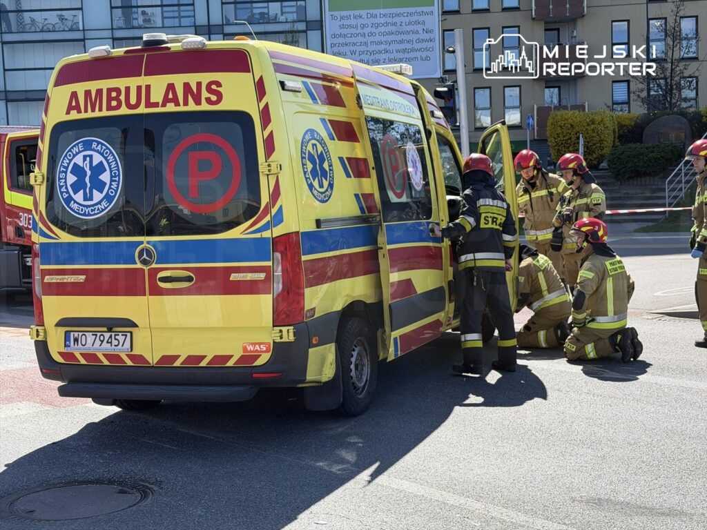 Zespół ratowników medycznych oraz strażaków pracuje przy ambulansie na miejskiej ulicy.
