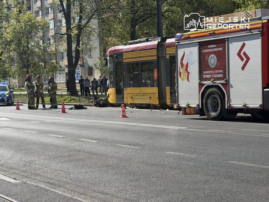 Grupa strażaków w mundurach rozmawia obok tramwaju, na jezdni leżą pachołki ostrzegawcze i torba.