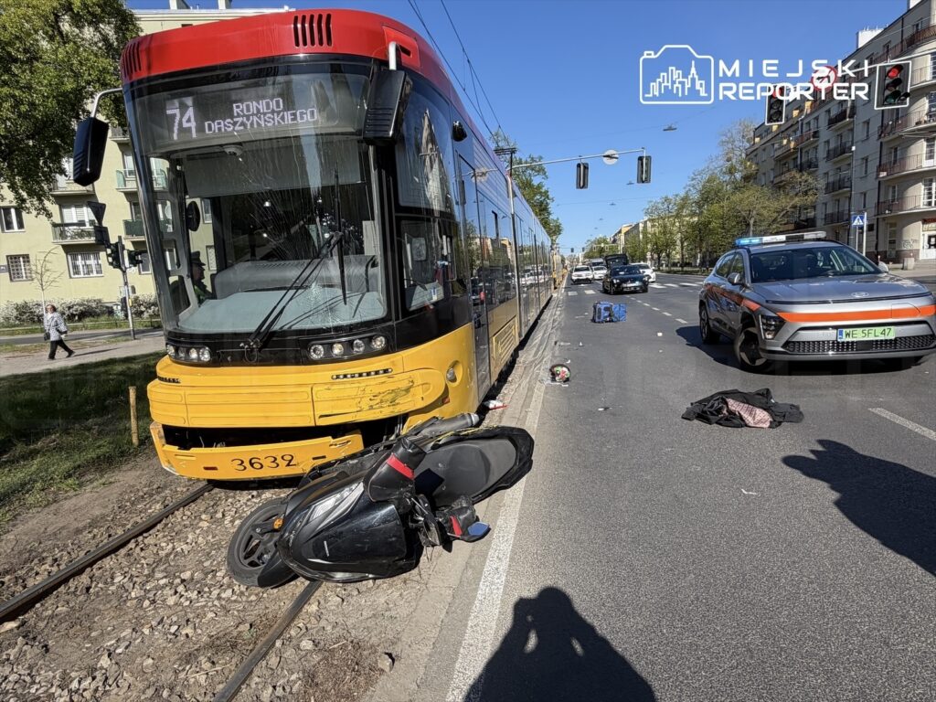 Zderzenie tramwaju z motocyklem na ulicy, obok leżące poszkodowane przedmioty oraz policyjny radiowóz.