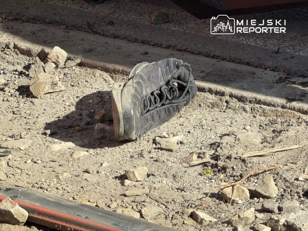 Czarny but sportowy leży na ziemi w okolicy budowy, otoczony kamieniami i gruzem.